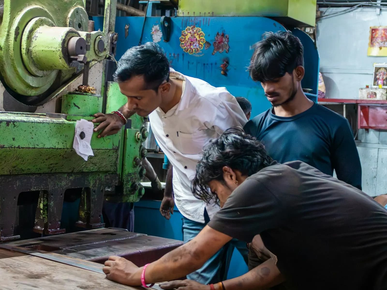 Workers lining up a metal sheet beside a power press in a small Indian workshop
