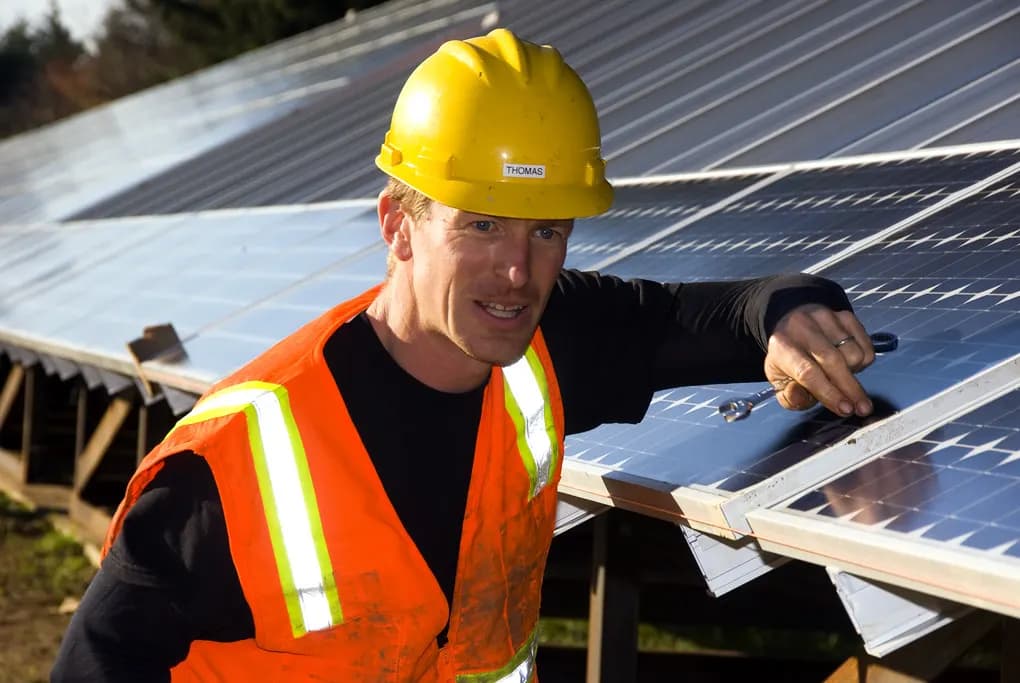 Installer in a hard hat and high-visibility vest fastening a solar module to a mounting rail
