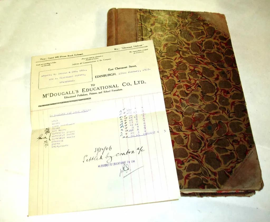 An old handwritten supplier invoice resting on a marbled-cover account ledger