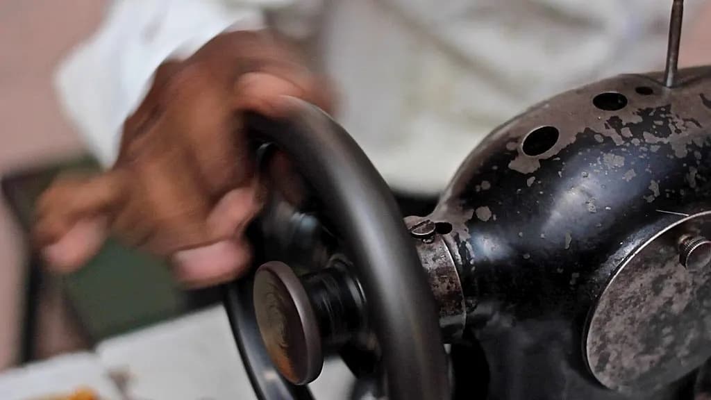 Close-up of a street tailor's hand turning the wheel of an old sewing machine in Bangalore