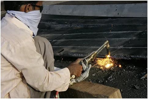 A worker cutting a steel plate with a gas torch in a fabrication workshop in Mandvi, Gujarat