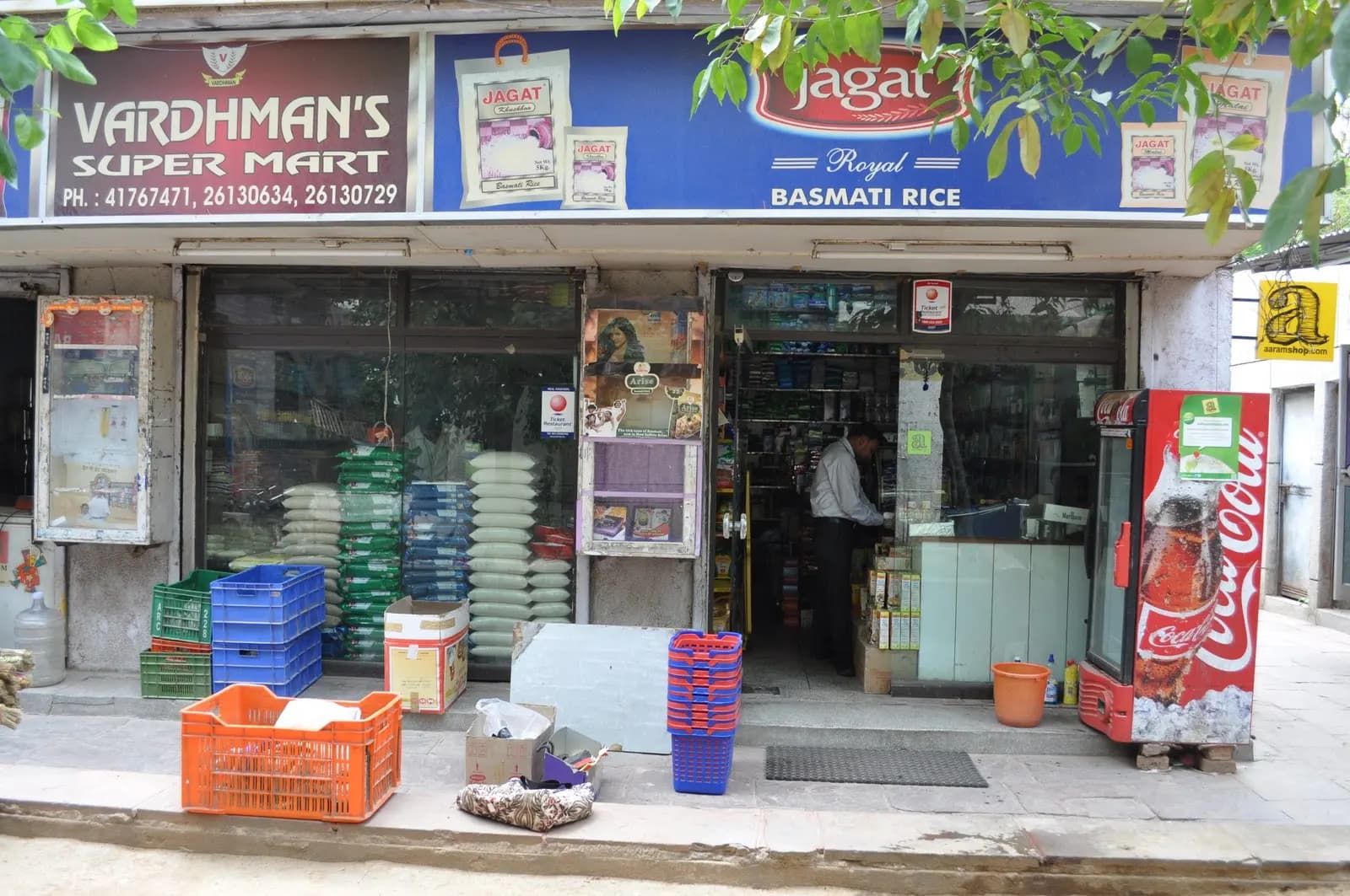 A neighbourhood kirana store front in India with rice sacks, crates and a cold-drinks fridge outside