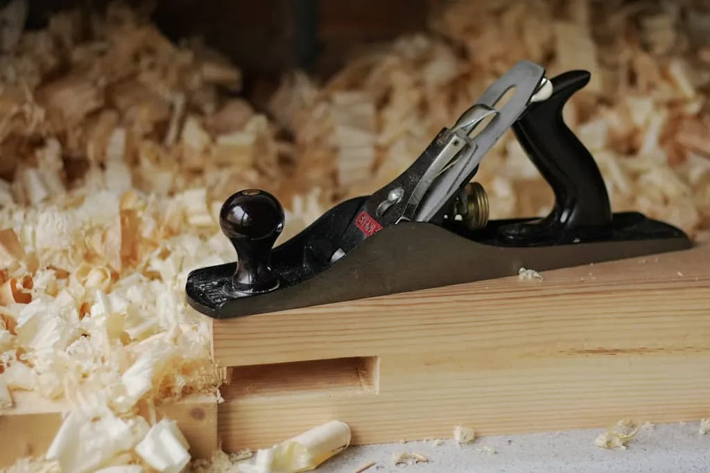 A metal hand plane resting on a length of timber surrounded by wood shavings on a workbench