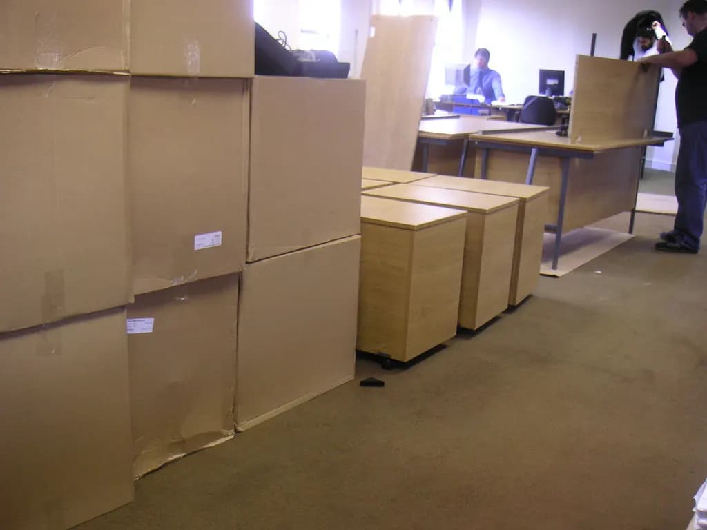 Packed cardboard boxes and desk pedestals stacked in an office being cleared