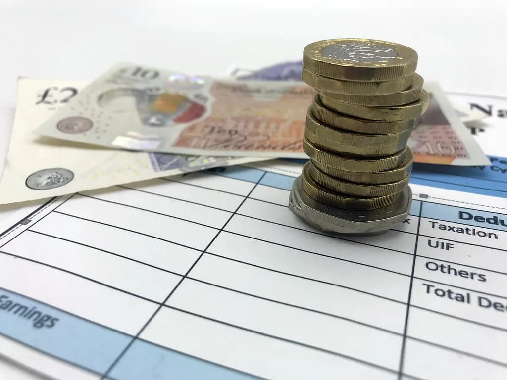 A stack of pound coins on a pay statement beside £10 and £20 notes