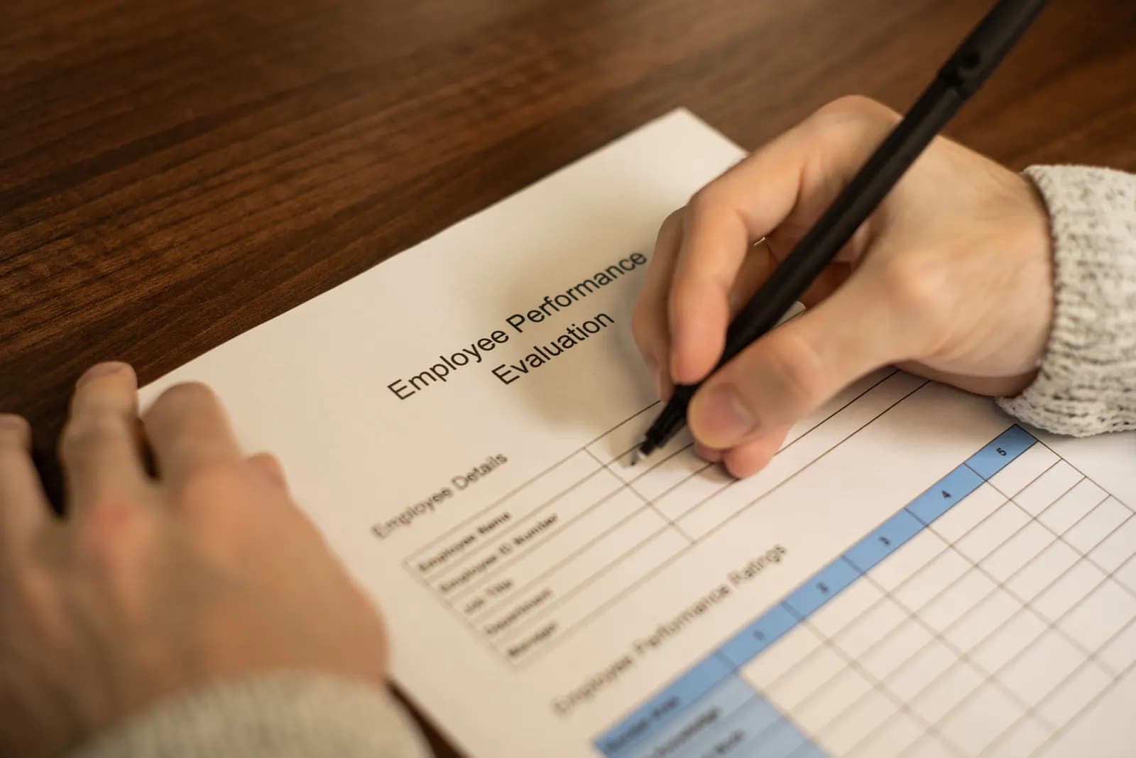 Close-up of a hand starting to fill in an employee performance evaluation form with a pen