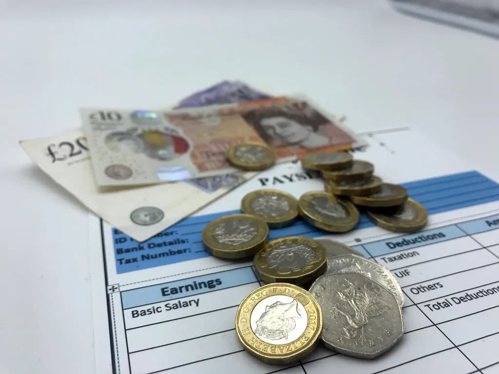 Pound coins and banknotes resting on a printed payslip showing earnings and deductions