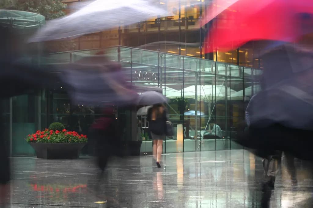 Office workers with umbrellas hurrying across a rainy plaza at Broadgate in the City of London
