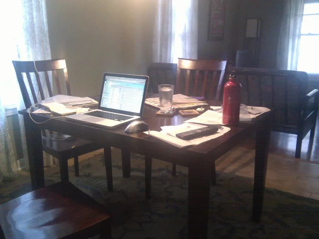 A laptop, mouse and papers set up on a dining table as a home workspace