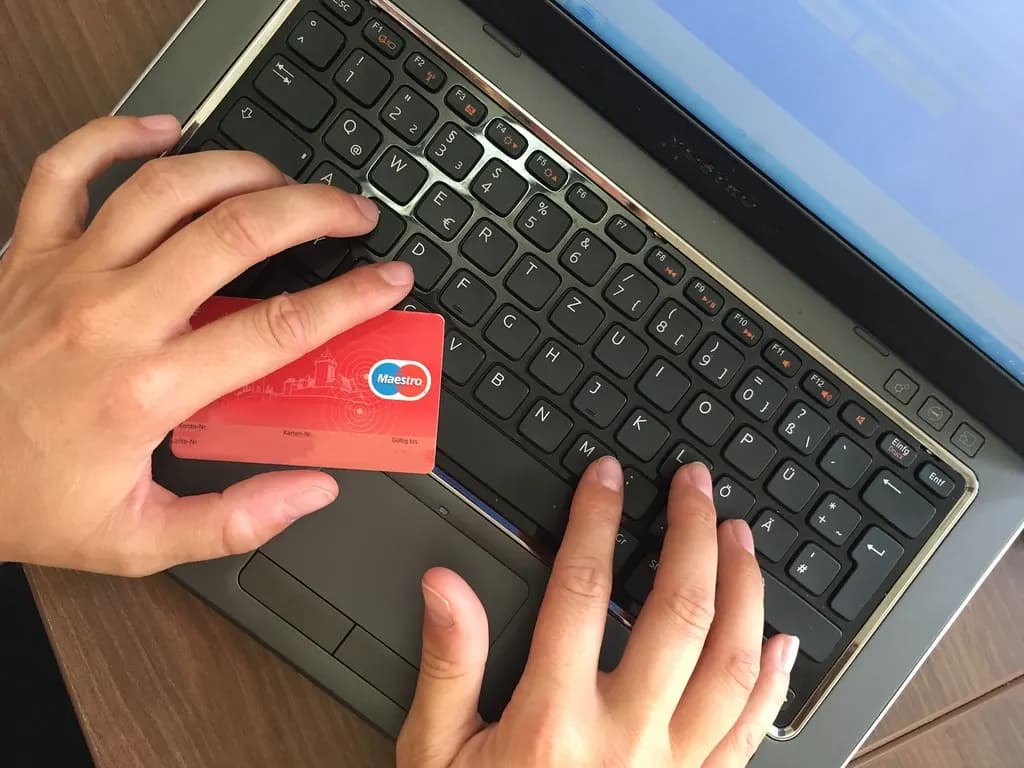A person typing on a laptop keyboard while holding a payment card