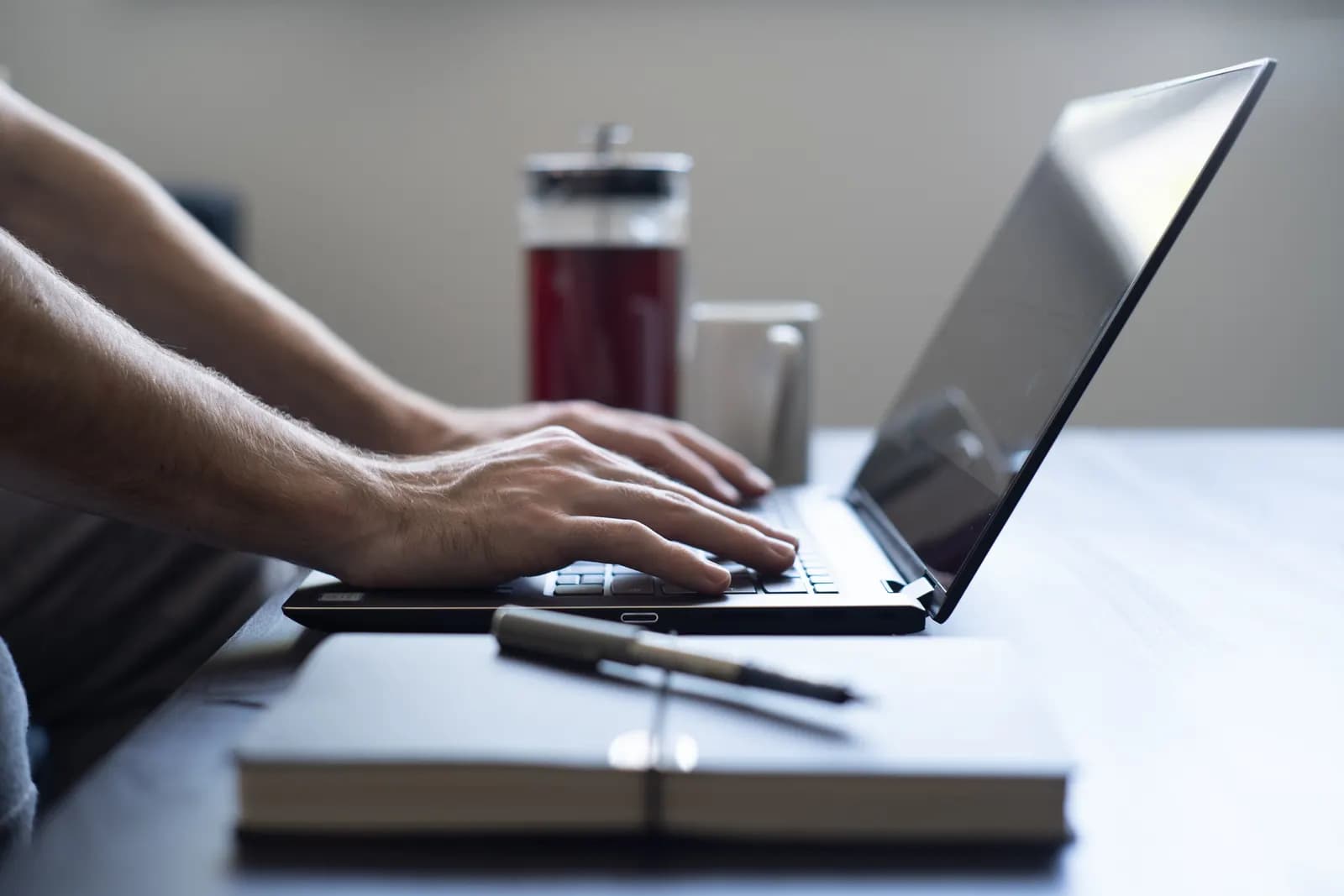 Sole trader typing on a laptop at a desk with a notebook and pen beside it