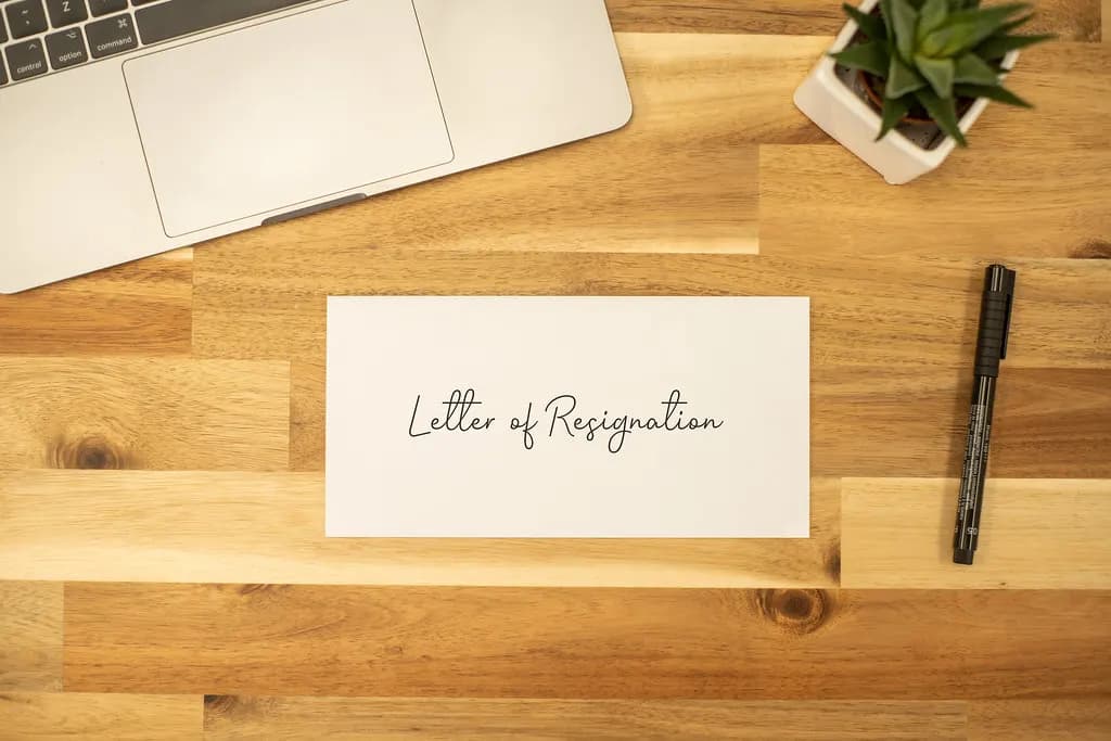 A handwritten letter of resignation in an envelope on a wooden desk beside a laptop and pen