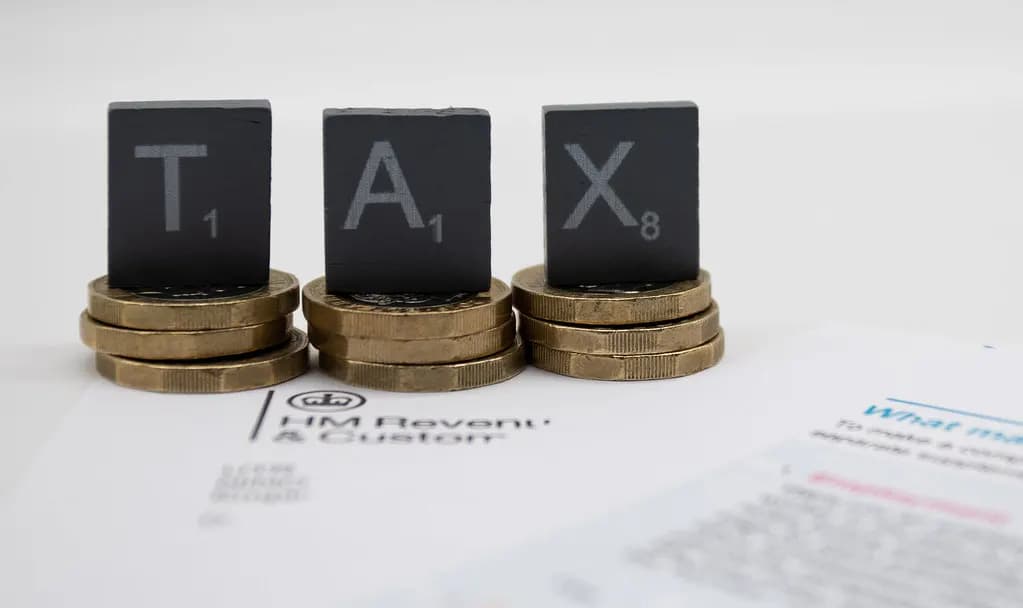 Letter tiles spelling TAX on stacks of pound coins resting on an HM Revenue and Customs letter