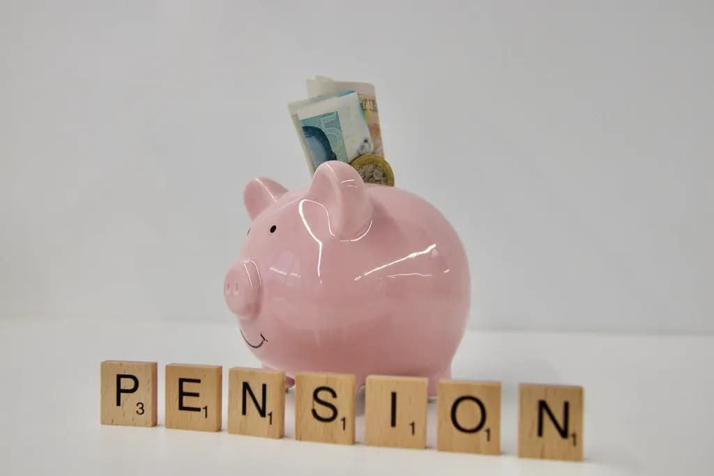 A pink piggy bank holding a banknote above wooden letter tiles spelling PENSION