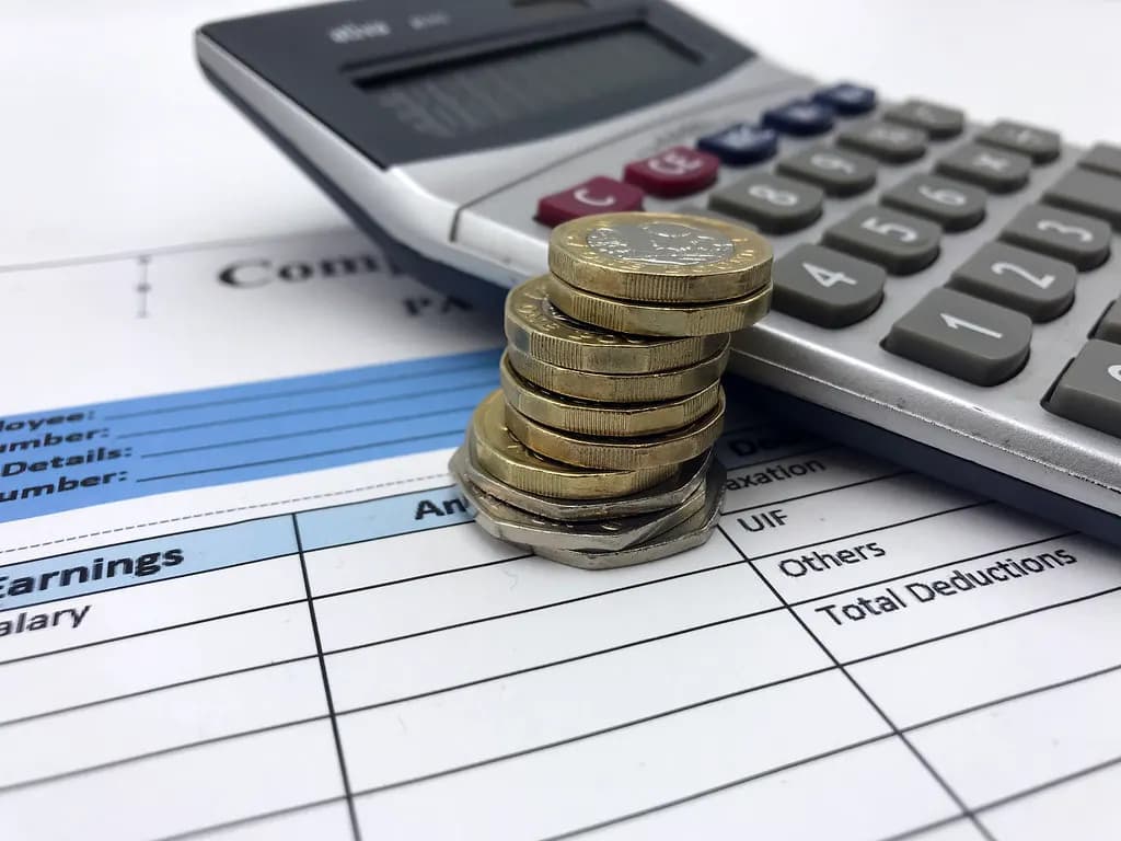 Stacks of pound coins and banknotes next to a calculator and a wage slip