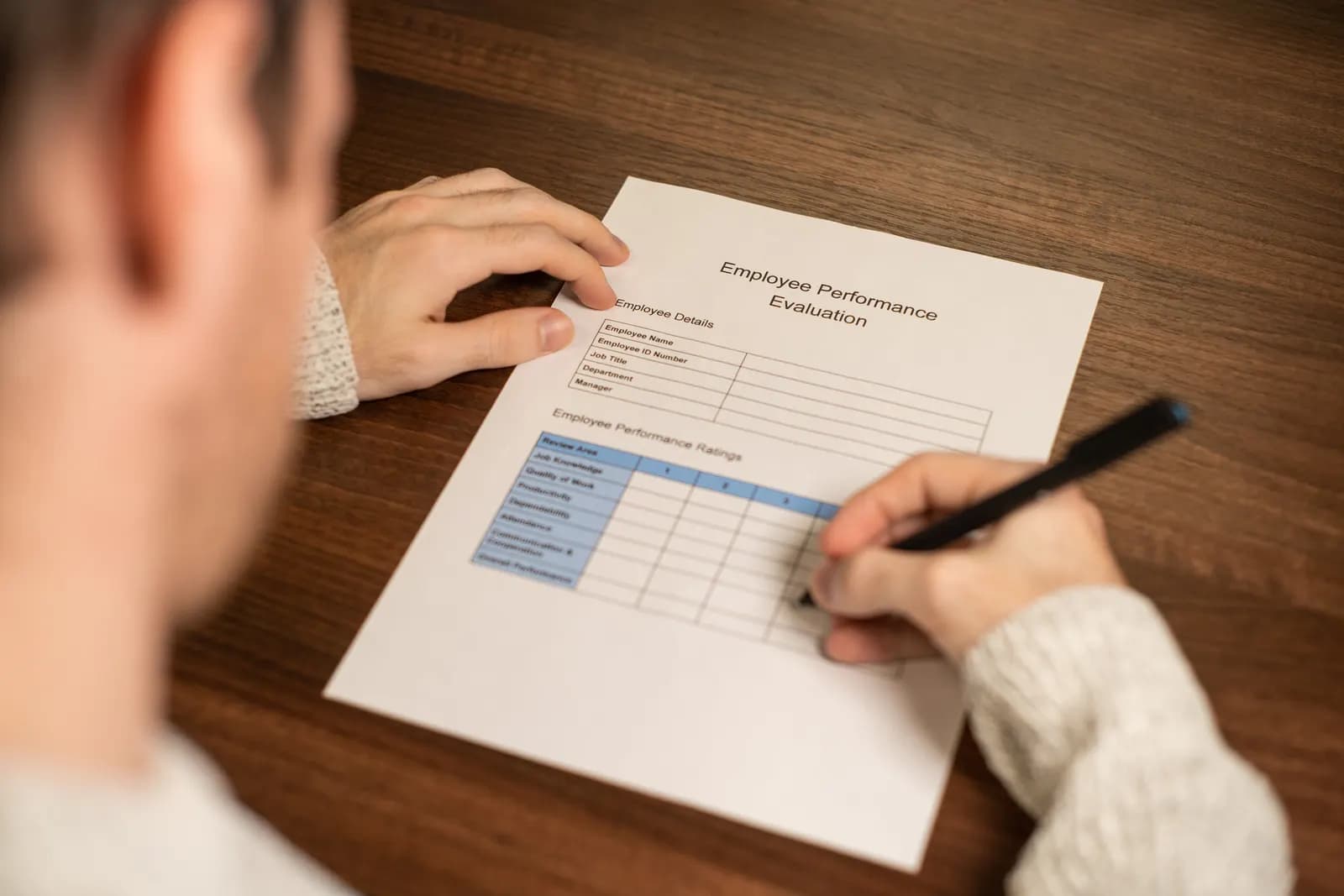A man sitting at a desk starting to fill in an employee performance review form