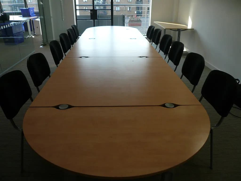 Long empty boardroom table surrounded by black chairs in a modern office meeting room