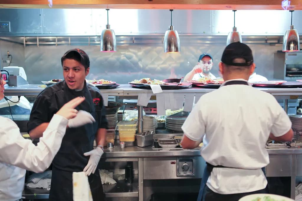 Chefs and kitchen staff working at the pass in a busy restaurant kitchen