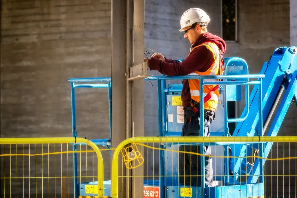 Electrician in a hard hat and hi-vis vest working from a mobile elevated work platform