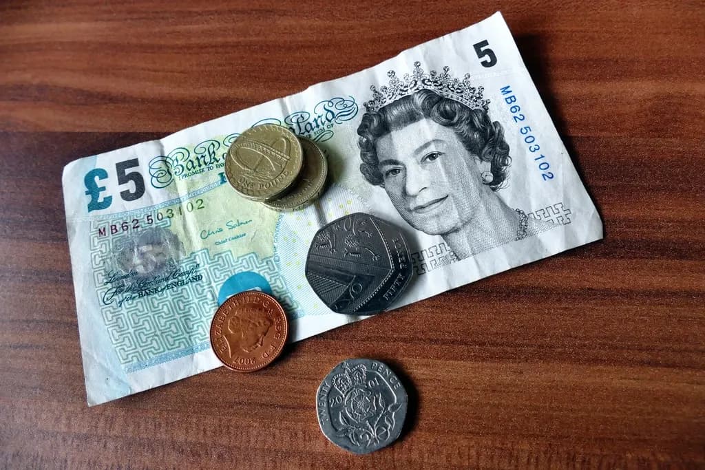 A five-pound note with one-pound, fifty, twenty and one pence coins on a wooden table