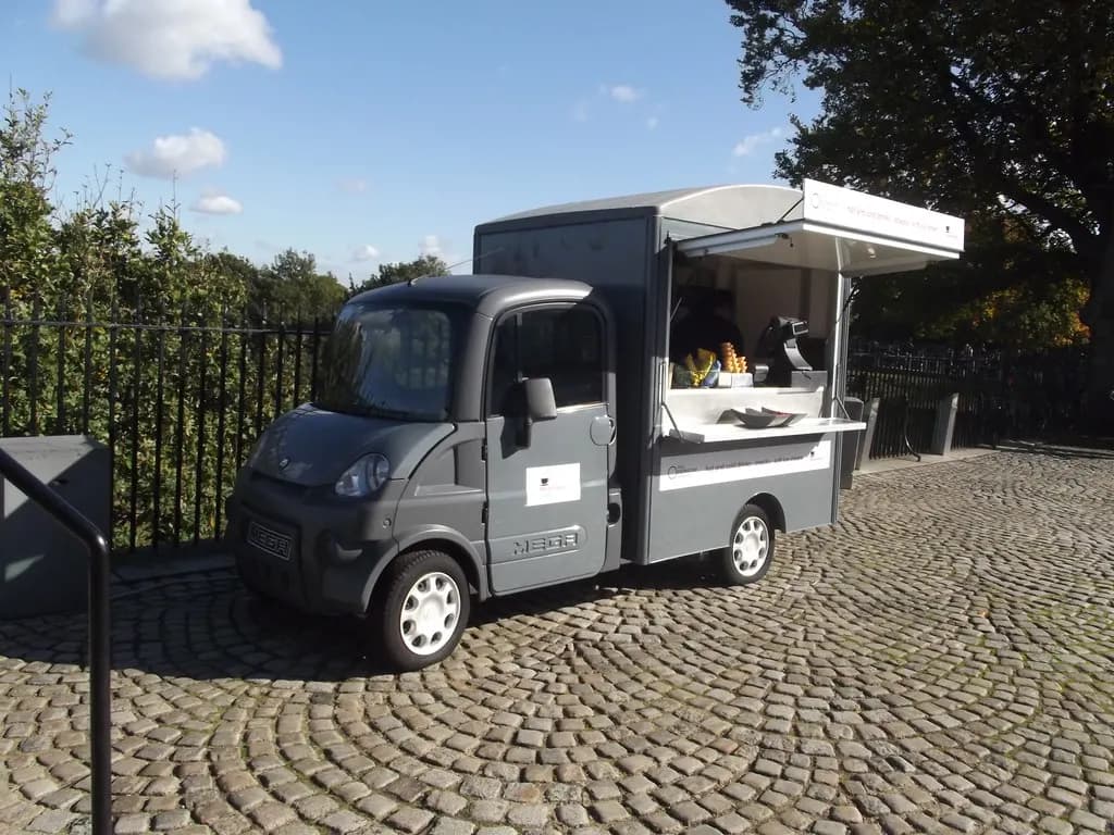A small electric food and coffee van parked on cobbles in Greenwich Park, London