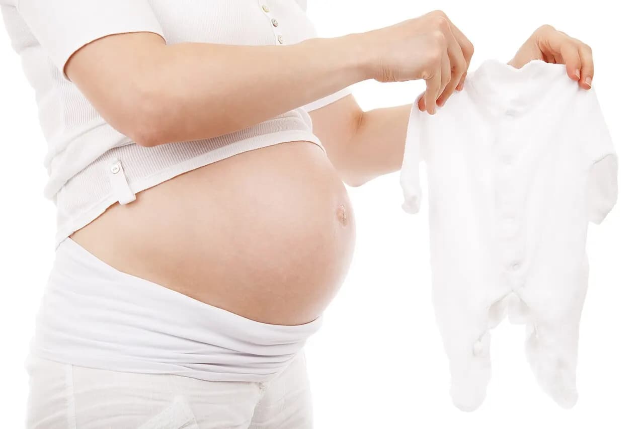 A pregnant woman holding up a small white babygrow
