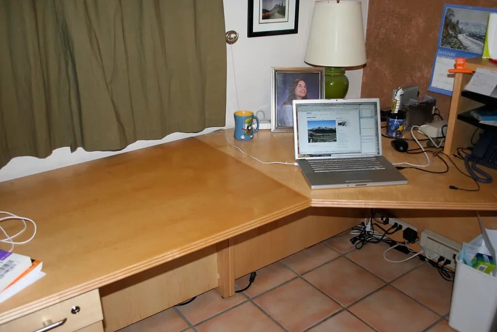 A cleared-out corner desk with a single open laptop, a lamp and a few cables left behind