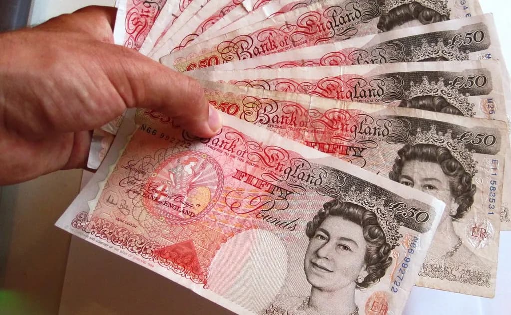 A hand holding a fan of Bank of England fifty-pound notes