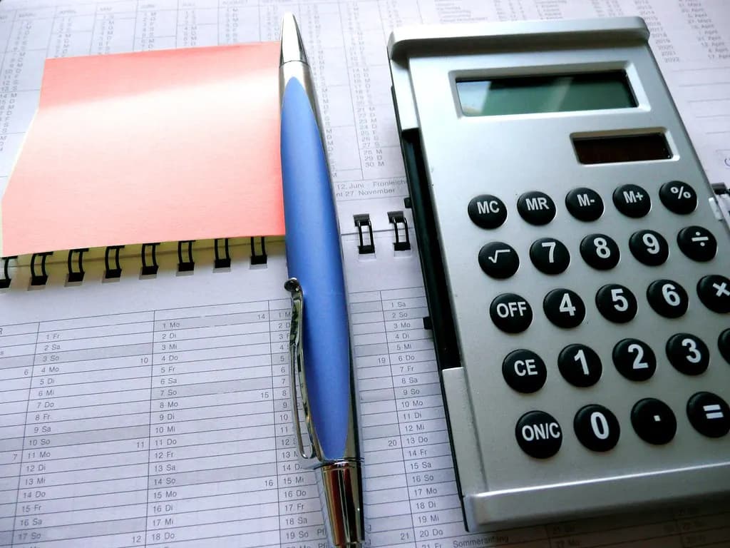 A calculator, a pen and a red sticky note on a desk