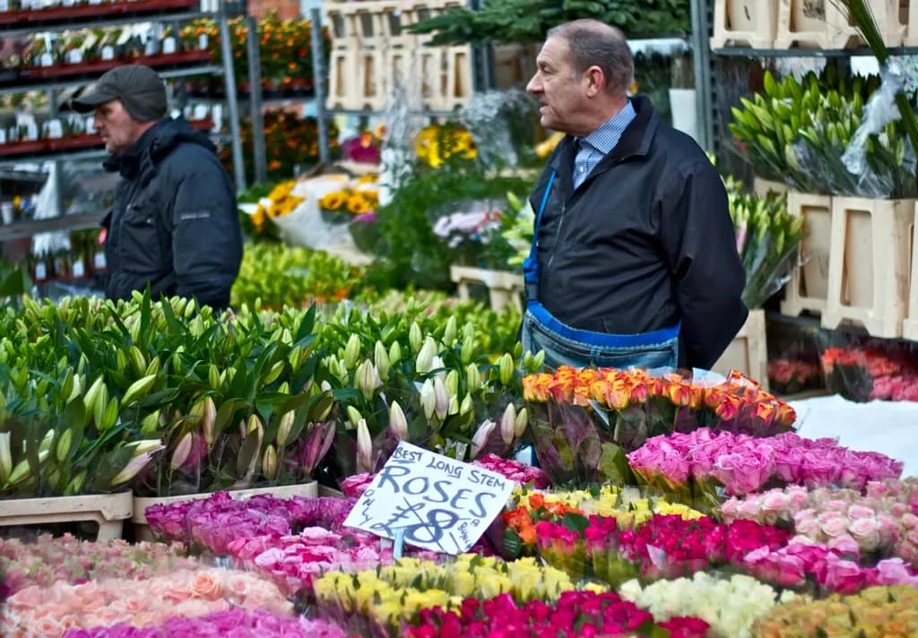 Flower sellers standing behind buckets of roses and tulips at Columbia Road Flower Market in east London