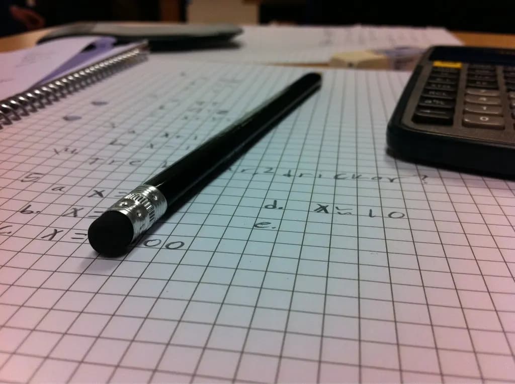 A pencil, calculator and squared paper with handwritten workings