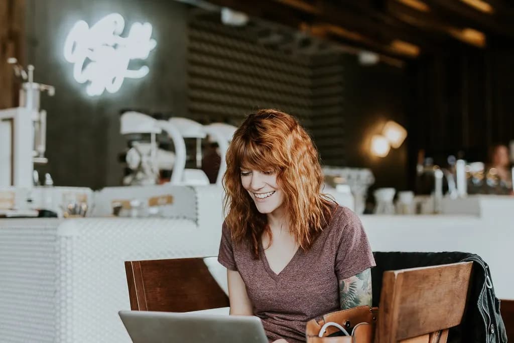 Freelancer smiling while working on a laptop at a cafe table