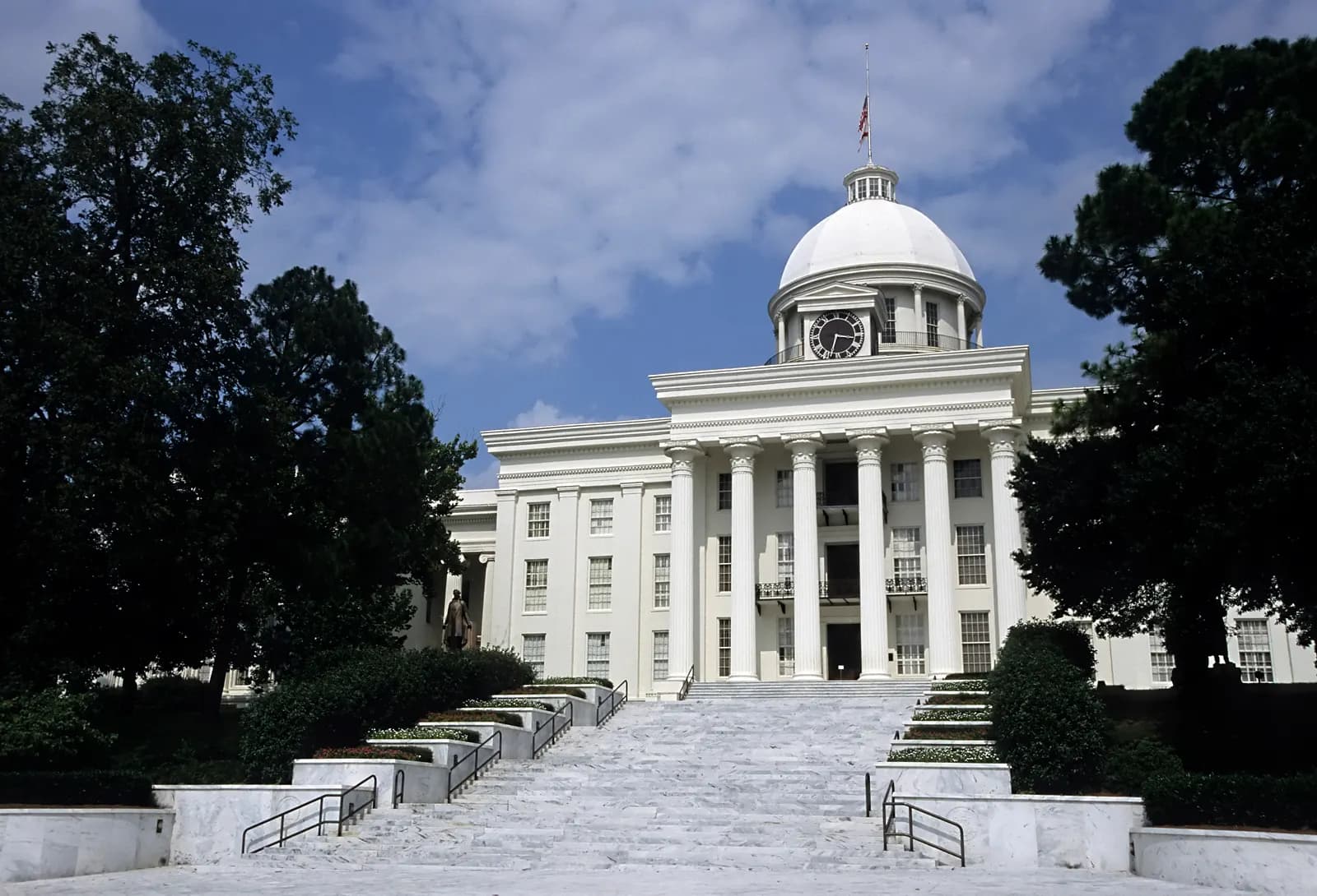 The white Alabama State Capitol in Montgomery, with its columned portico and dome, seen from the front lawn