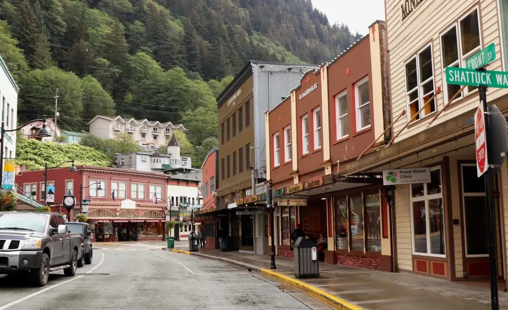 Shops in painted wooden buildings on a street in downtown Juneau, Alaska, below forested mountains