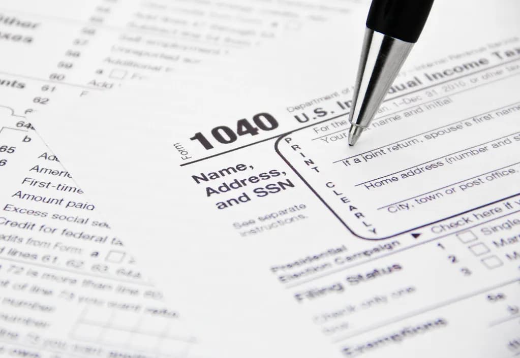 Close-up of a paper IRS Form 1040 individual income tax return with a pen pointing at the name and address box
