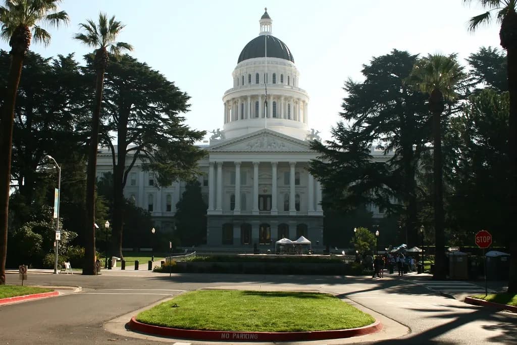 The white domed California State Capitol in Sacramento framed by palms and a circular lawn