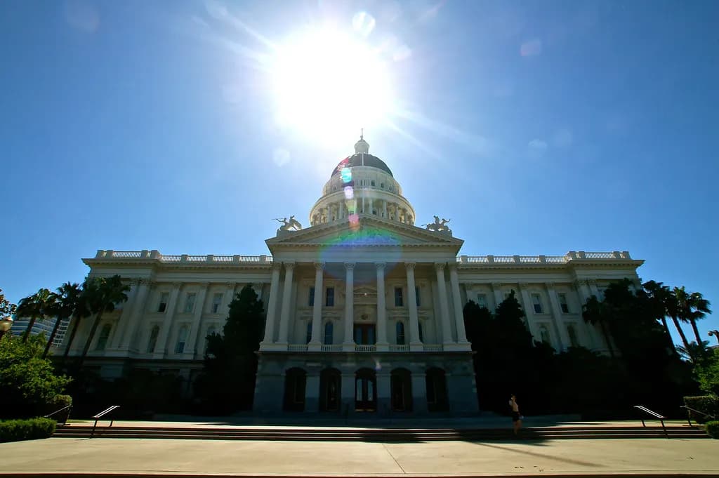 The California State Capitol in Sacramento with its white dome and columned facade behind palm trees