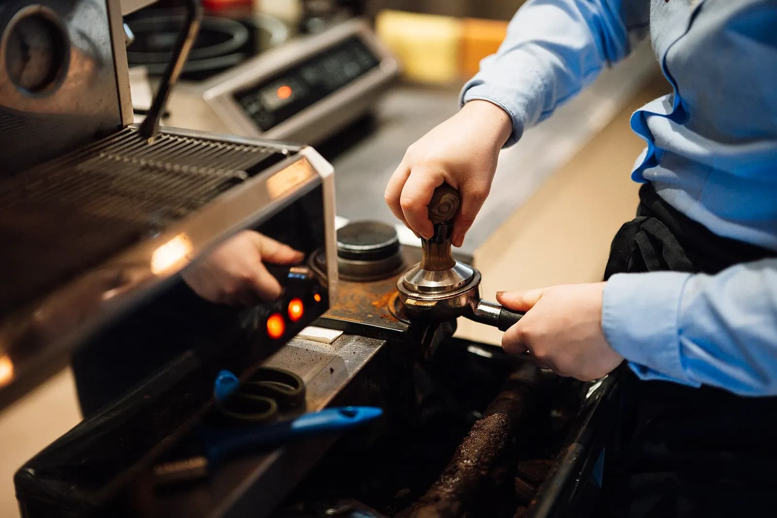 Barista tamping coffee grounds into a portafilter at a café espresso machine