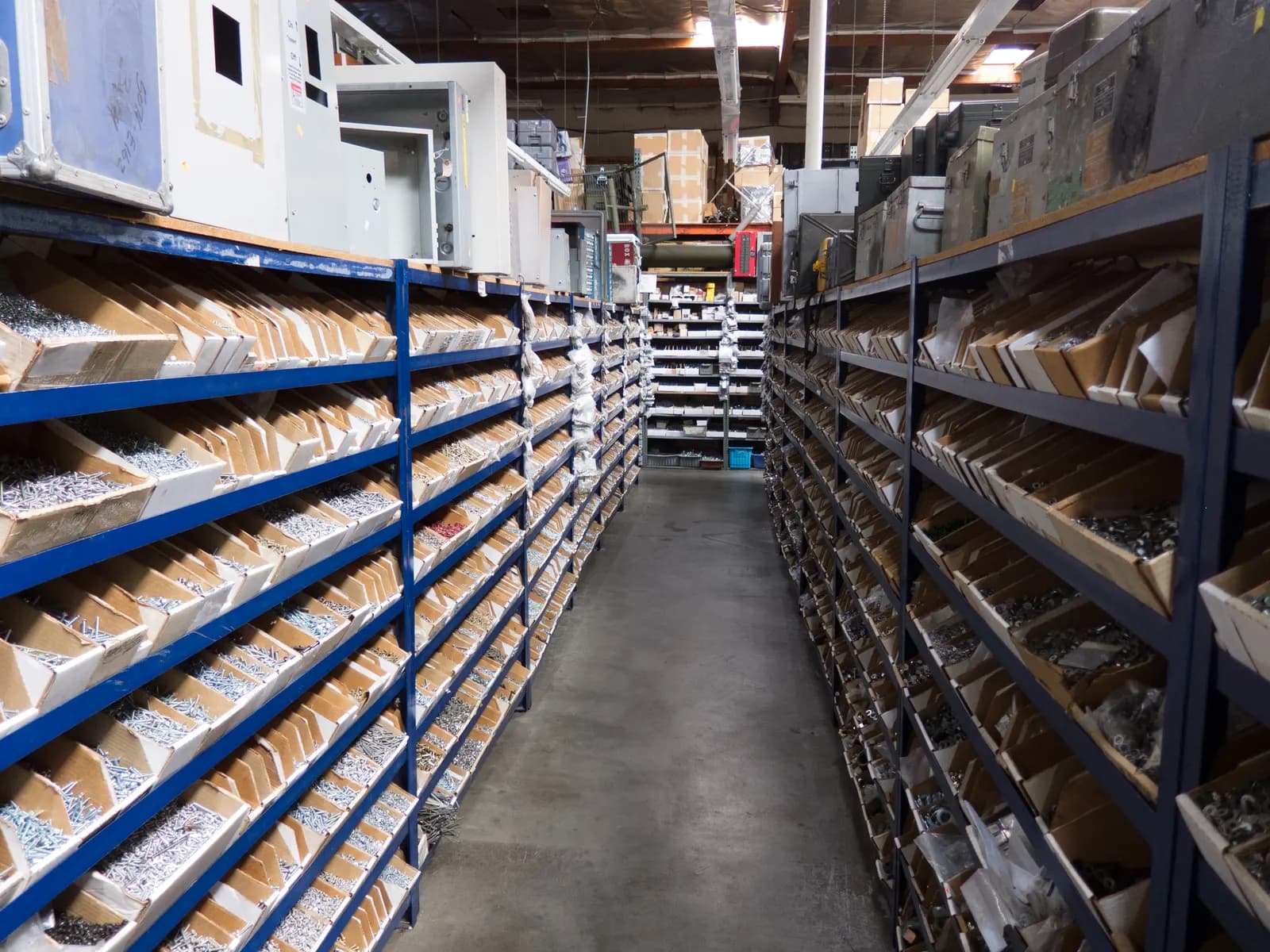 Long aisle of shelving with hundreds of labeled bins of screws, fasteners and small hardware parts