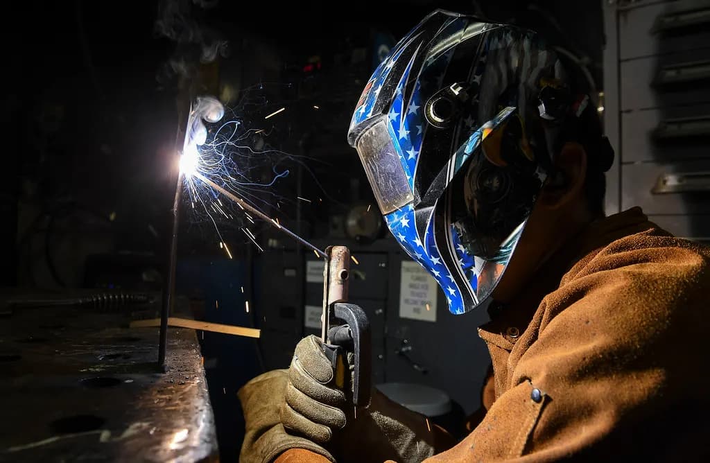 Welder in a decorated welding helmet and leather jacket welding metal, with sparks flying