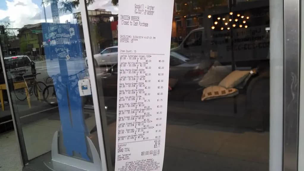 Long itemized store receipt taped to a shop window showing item prices and a grand total