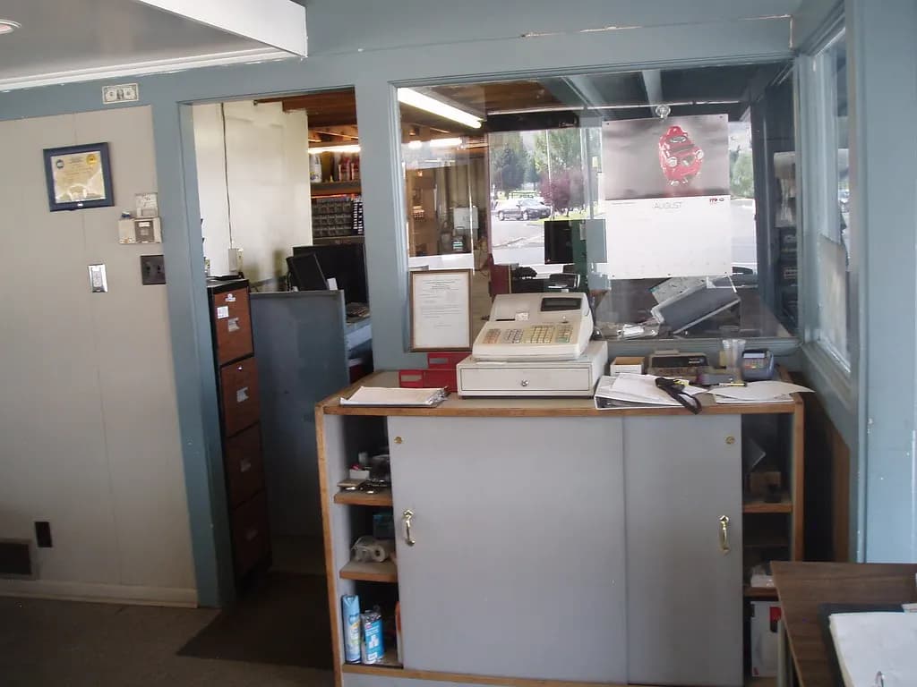 Small business front counter with a cash register and paperwork behind a service window