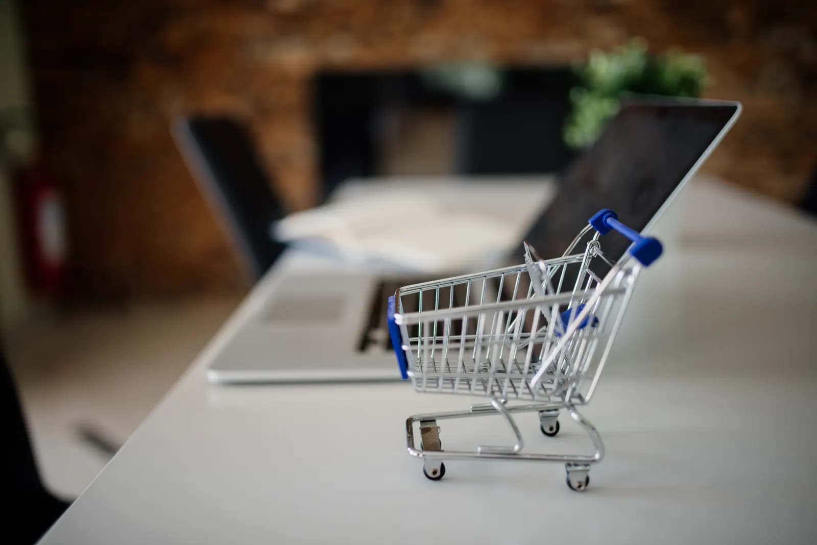 Miniature shopping cart on a desk beside an open laptop