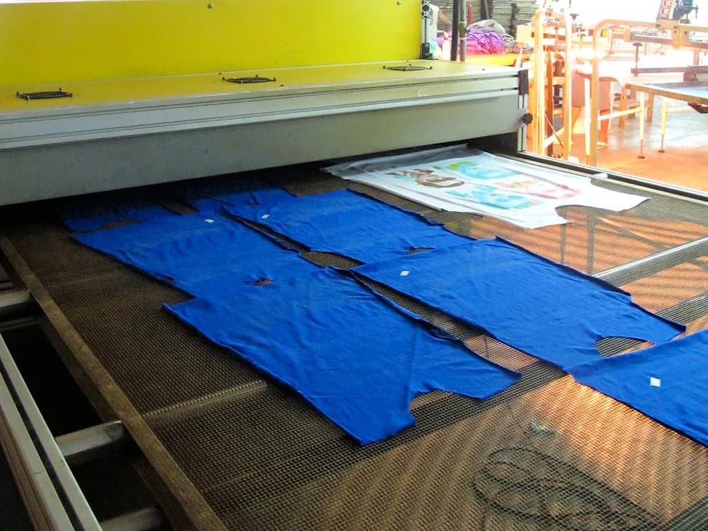 Blue printed T-shirts moving through a conveyor dryer in a screen printing shop