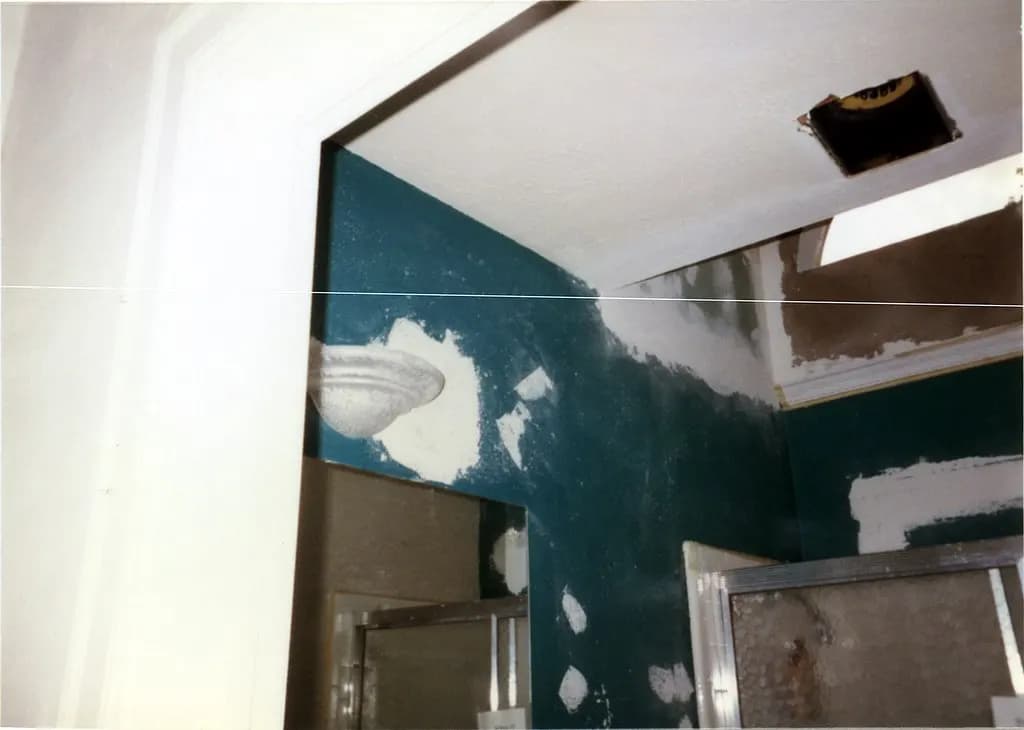 Bathroom under renovation with freshly patched drywall, an open ceiling vent and old wall tile partly removed
