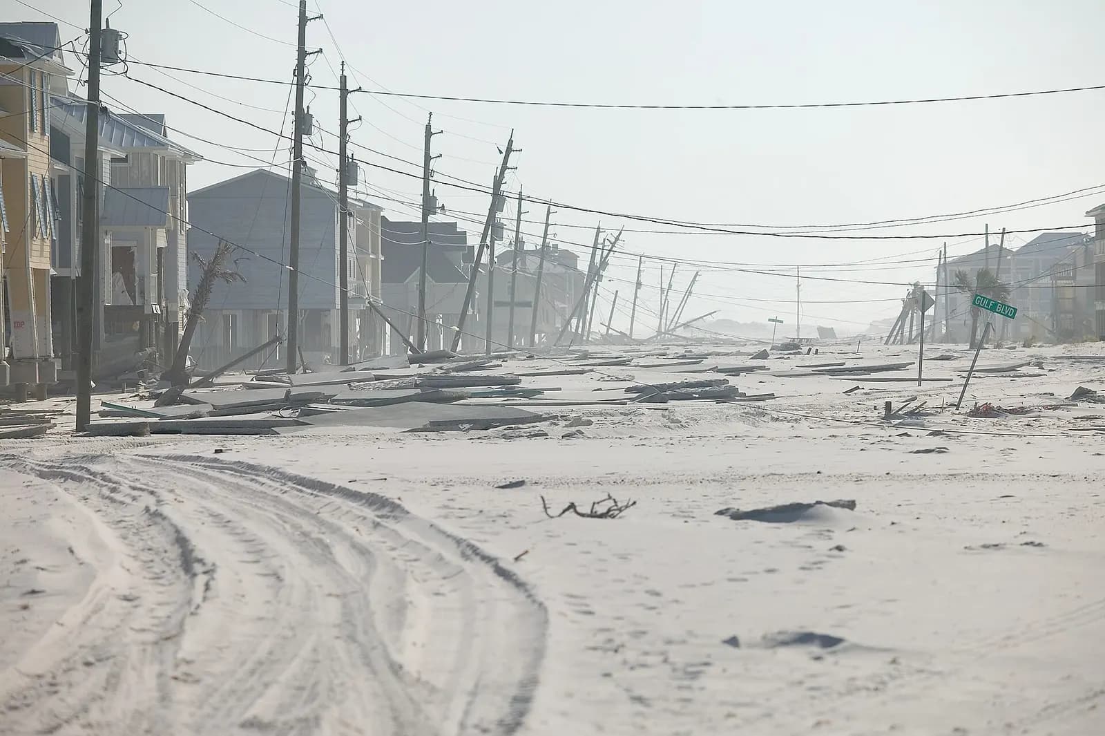 Sand-covered road lined with leaning utility poles and damaged buildings in Navarre Beach, Florida after Hurricane Dennis