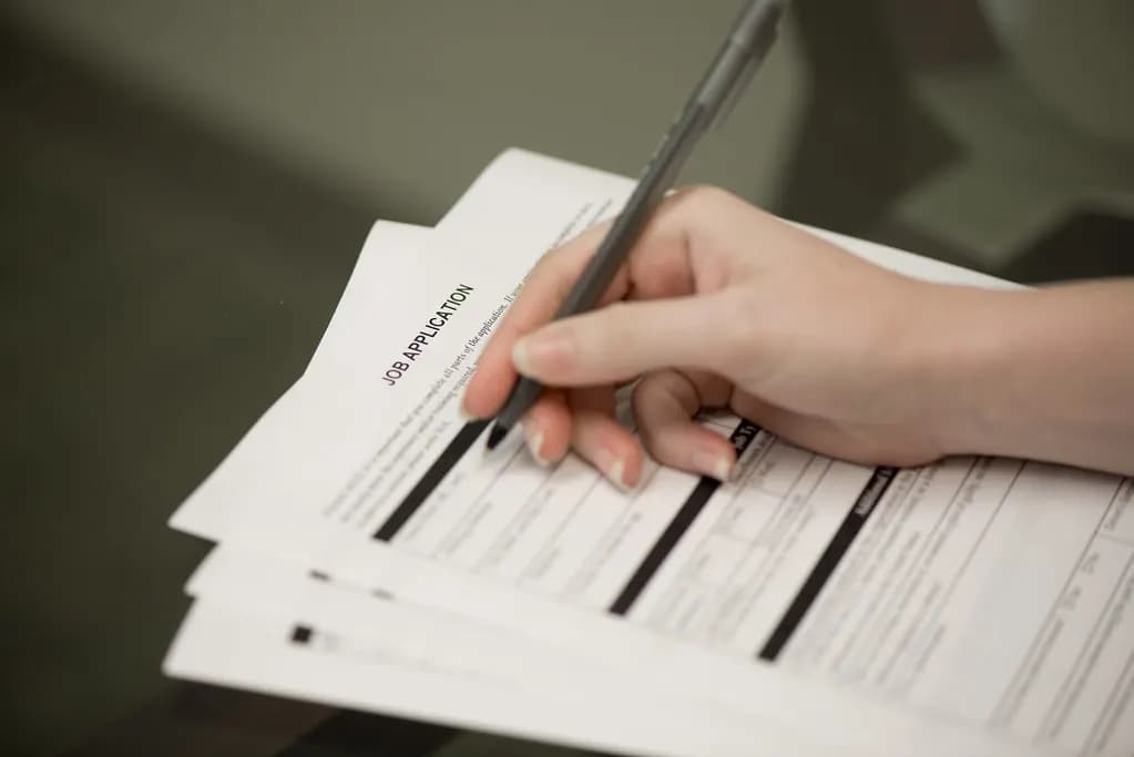 Hand holding a pen filling out a printed job application form on a desk