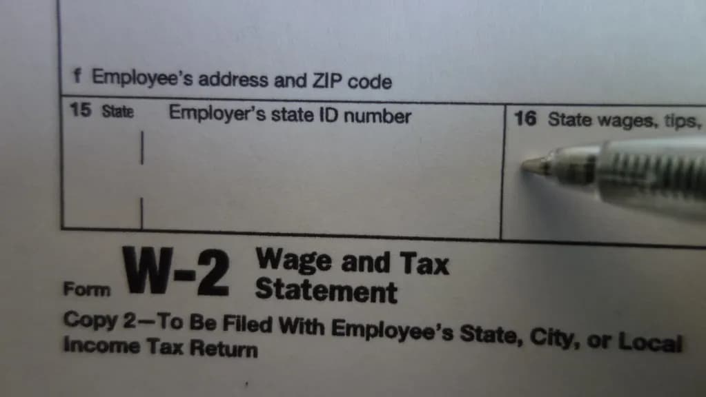 Close-up of a Form W-2 Wage and Tax Statement showing box 15 state and employer's state ID number and box 16 state wages, with a pen