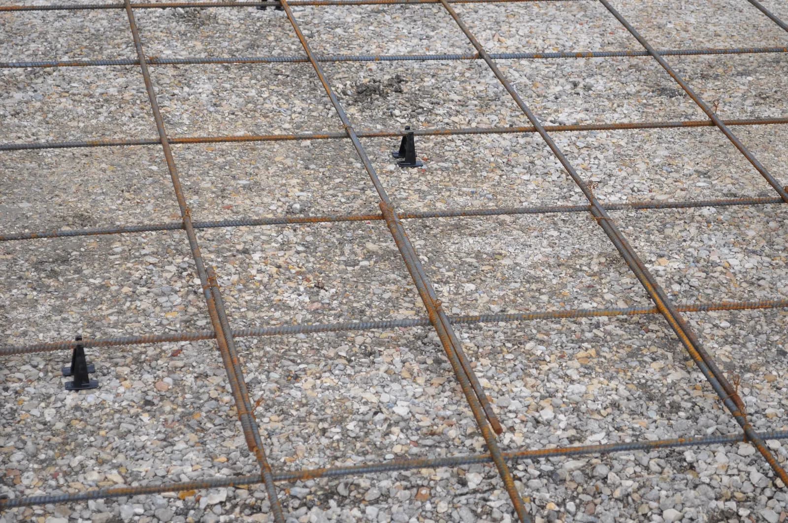 A grid of steel rebar on plastic chairs over a compacted gravel base, ready for a concrete driveway pour