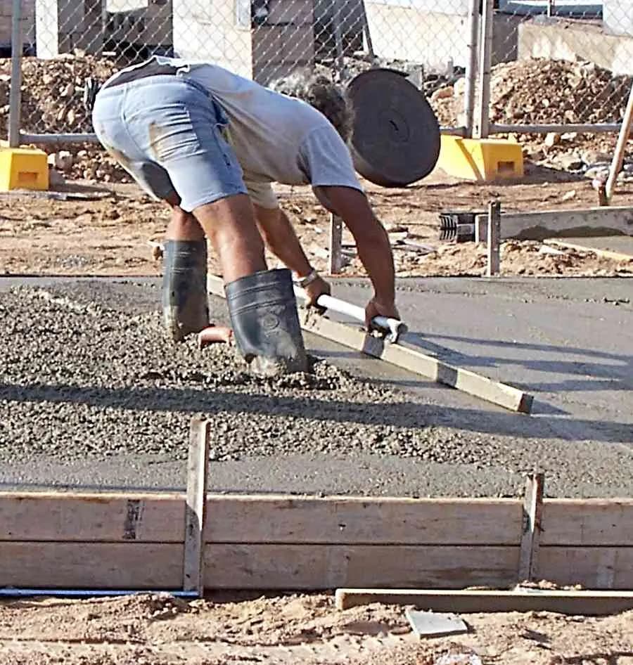 A worker drawing a straightedge screed across freshly placed concrete inside wooden slab forms